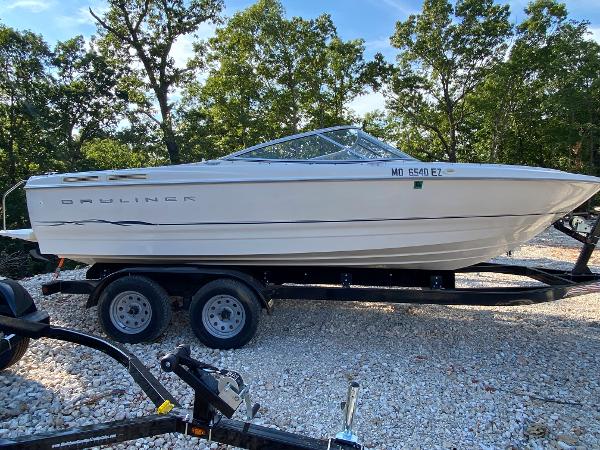 Slide: The Image of 2001 Bayliner 215 Bowrider on a trailer, parked on gravel, surrounded by trees. - 0