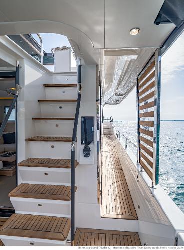Slide: The Image of 2025 Beneteau Grand Trawler 62 yacht, featuring elegant wooden stairs and deck, ocean view. - 10