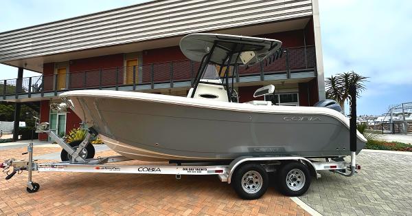 Slide: The Image of 2023 Cobia Center Console 220 boat on a trailer in front of a modern building. - 1
