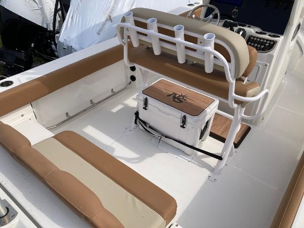 Slide: The Image of 2023 NauticStar 24 Legacy boat interior with tan and white seating, rod holders, and cooler. - 3