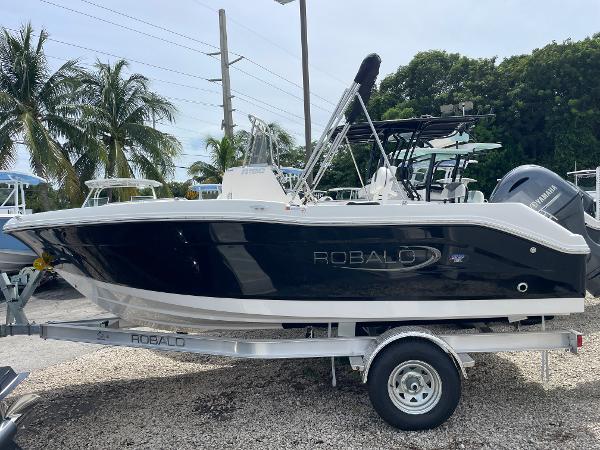 Slide: The Image of 2023 Robalo R180 Center Console boat on trailer, surrounded by palm trees. - 0