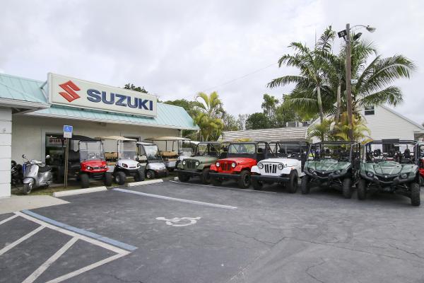 Slide: The Image of Outdoor display of Suzuki vehicles at dealership, featuring various models under palm trees. - 47