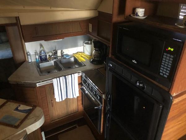 Slide: The Image of 1983 Sea Ray 390 Sport Fisherman kitchen with sink, stove, microwave, and wooden cabinets. - 21